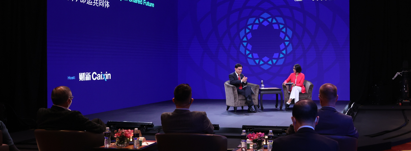 On-stage interview with Caixin backdrop, man and woman in chairs, audience in foreground.